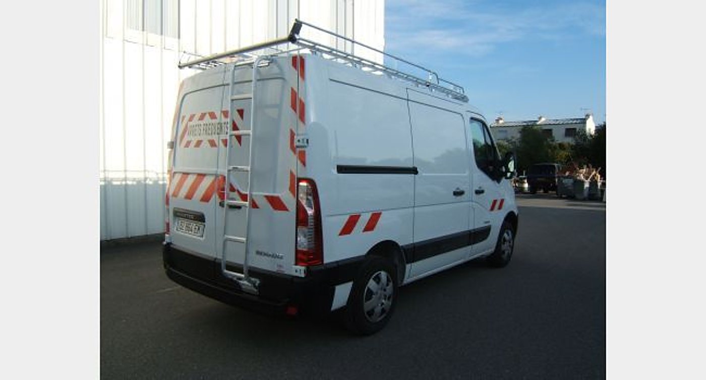 Une camionnette utilitaire blanche avec galerie de toit, échelle arrière et bandes rouges et blanches, garée sur un parking goudronné.