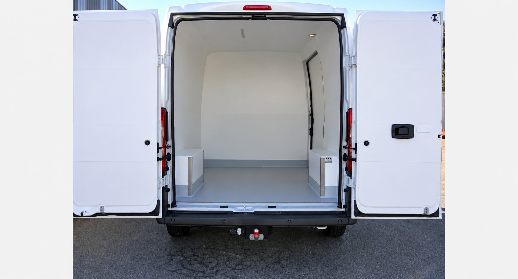 Vue arrière d'un fourgon utilitaire blanc dont les portes sont ouvertes, révélant un compartiment de chargement isolé avec sol gris et deux coffrages latéraux.