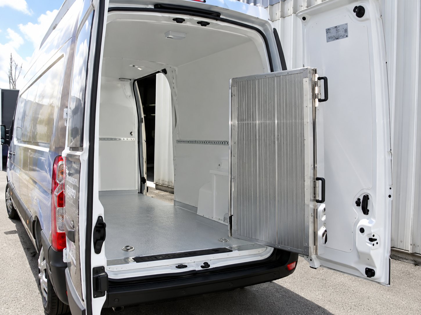 Vue de l'espace de chargement vide et revêtu d'un fourgon utilitaire blanc dont les portes arrière sont ouvertes.