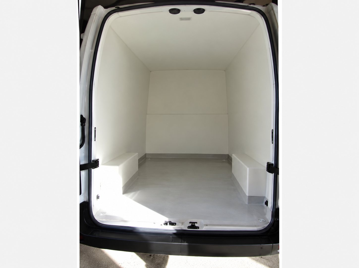 Vue de l'intérieur d'un fourgon utilitaire vide dont les parois et le plancher sont recouverts d'un revêtement blanc.