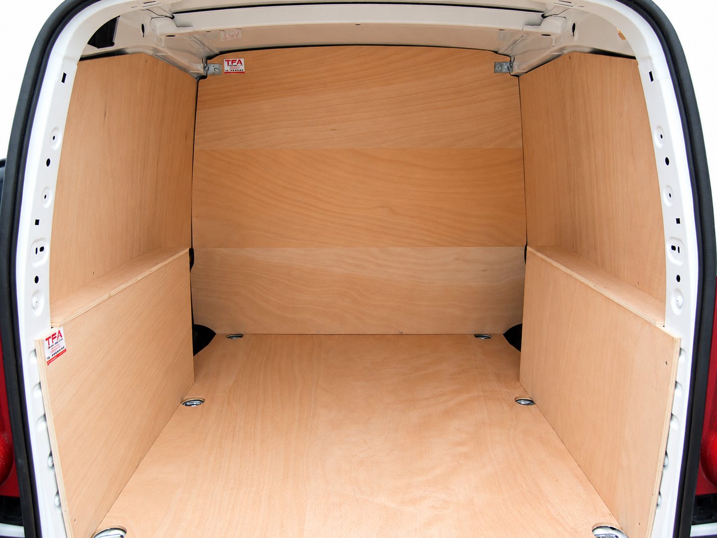 Vue arrière de l'espace de chargement d'une camionnette blanche dont le sol et les parois sont recouverts de panneaux de contreplaqué.