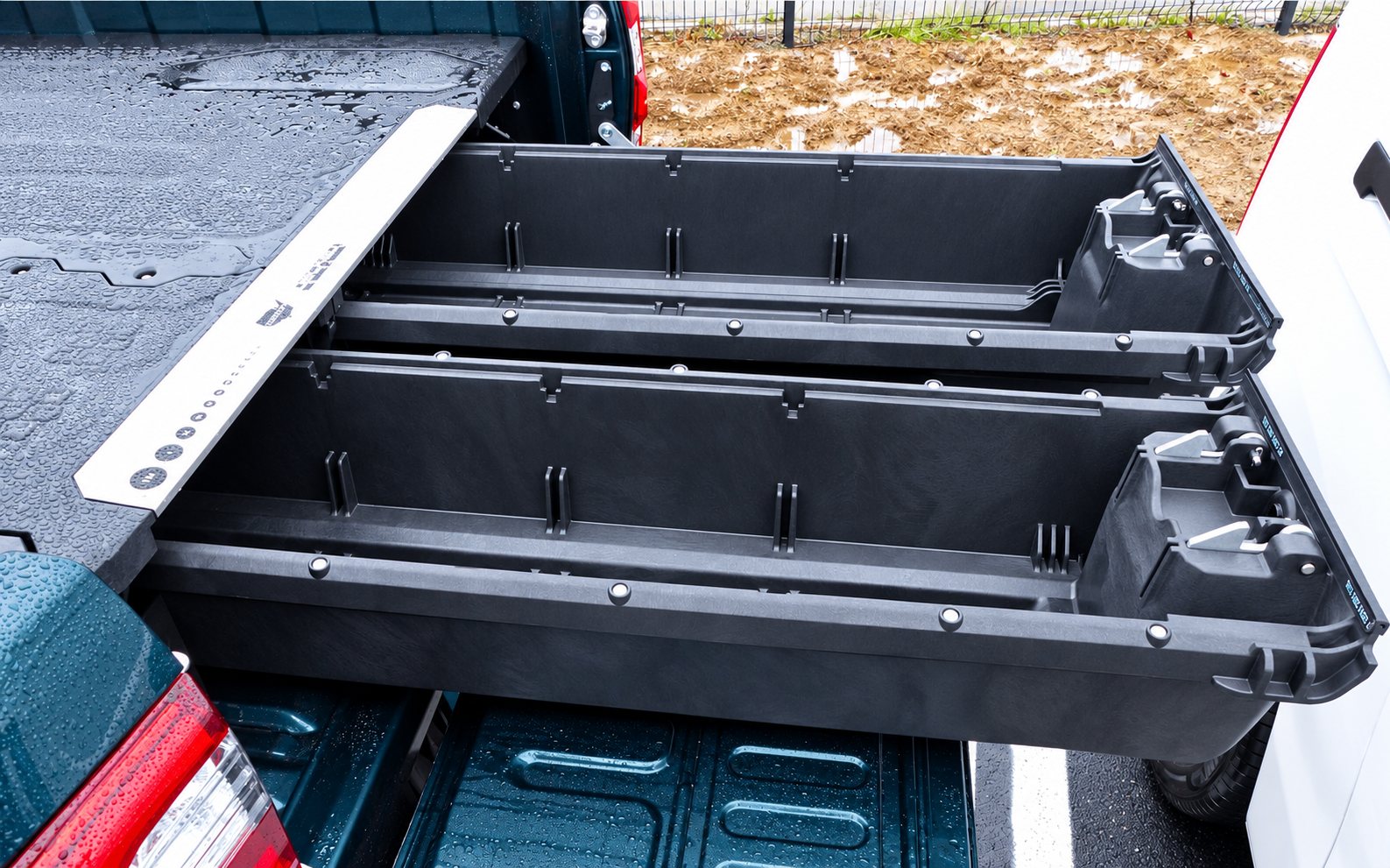 Deux tiroirs de rangement noirs en plastique sortis à moitié de la benne d'un pick-up vert, sur un parking humide.